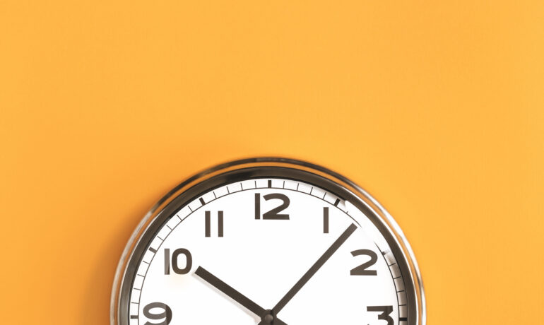 Part of analogue plain wall clock on trendy pastel orange background. Ten o'clock.