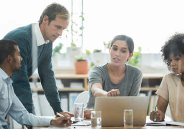 Stock photo of four diverse people sitting and standing around a computer screen